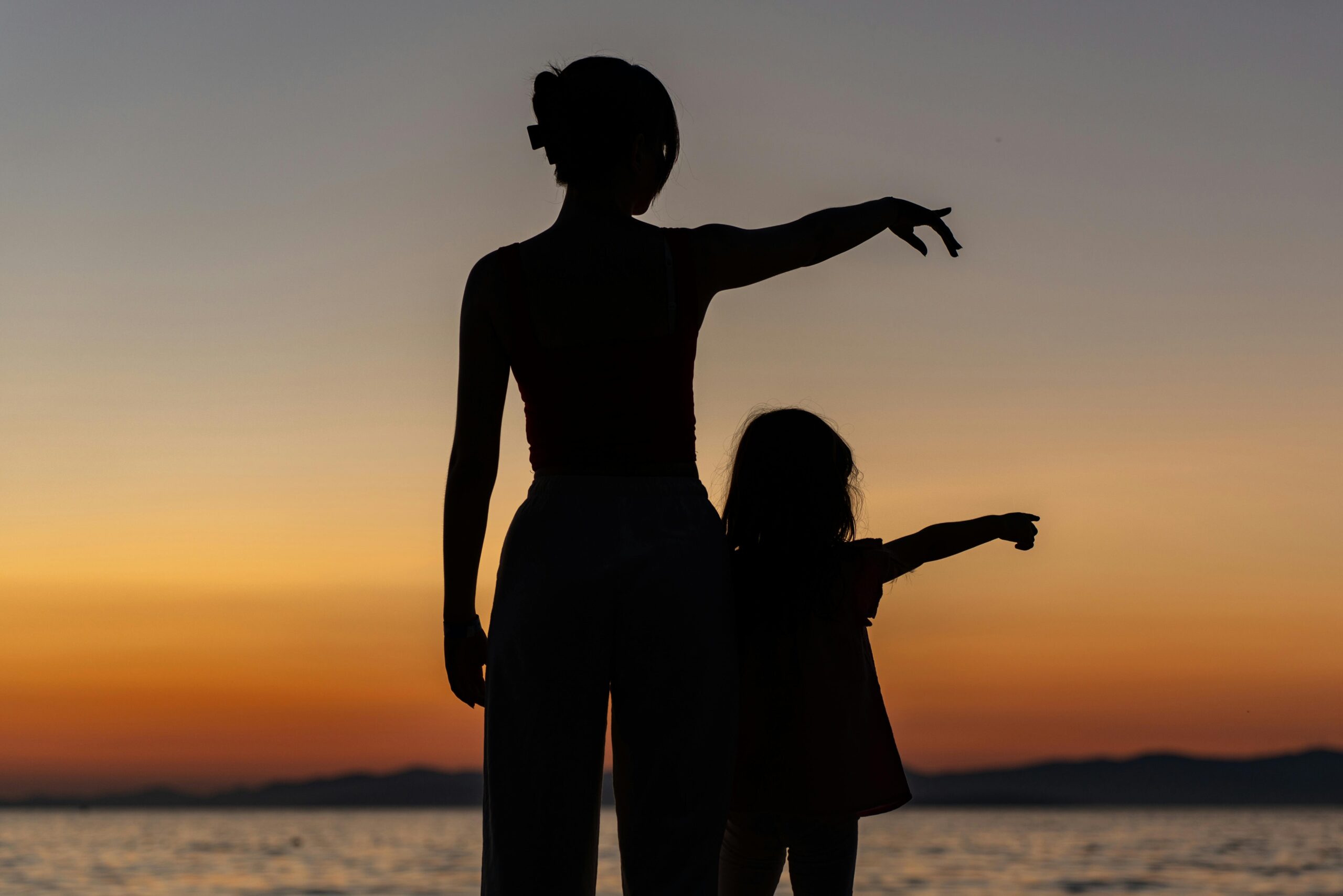 A woman and child standing on the beach at sunset